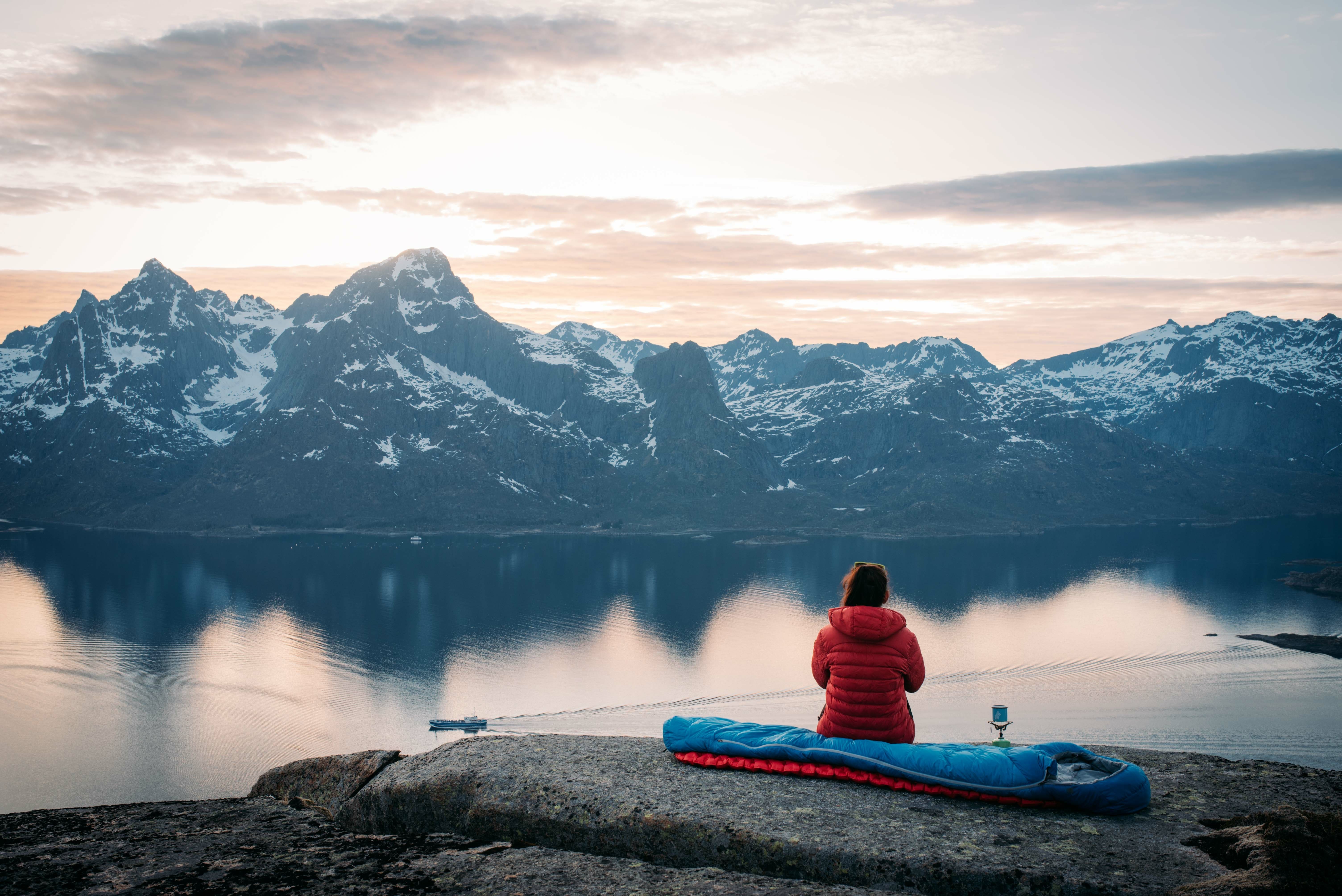woman watches mountain scenery while sitting in sleeping bag