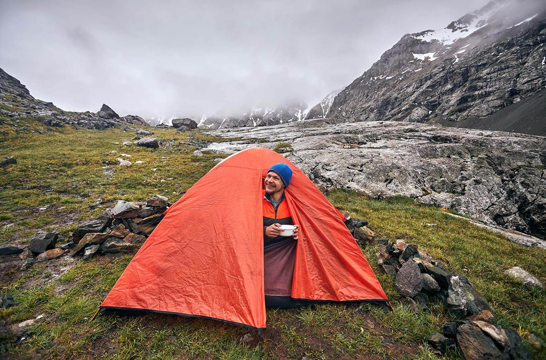 man watches rain from inside tent